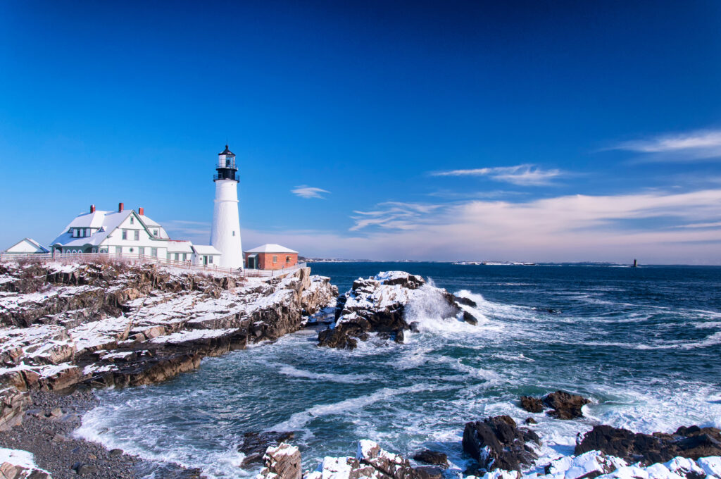 the iconic landmark Portland Headlight after a winter storm in Portland Maine on a sunny blue sky day.